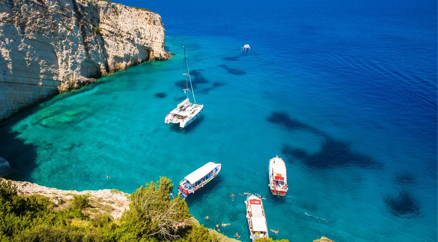 Aerial view of excursion boats and a catamaran anchored in a turquoise cove beneath white cliffs