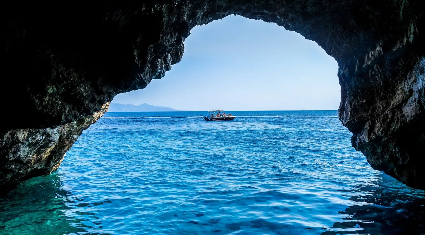 The mouth of a sea cave framing a small tour boat on open blue water beyond