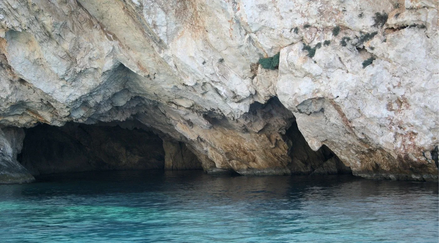 A dark cave entrance at the waterline beneath layered white limestone