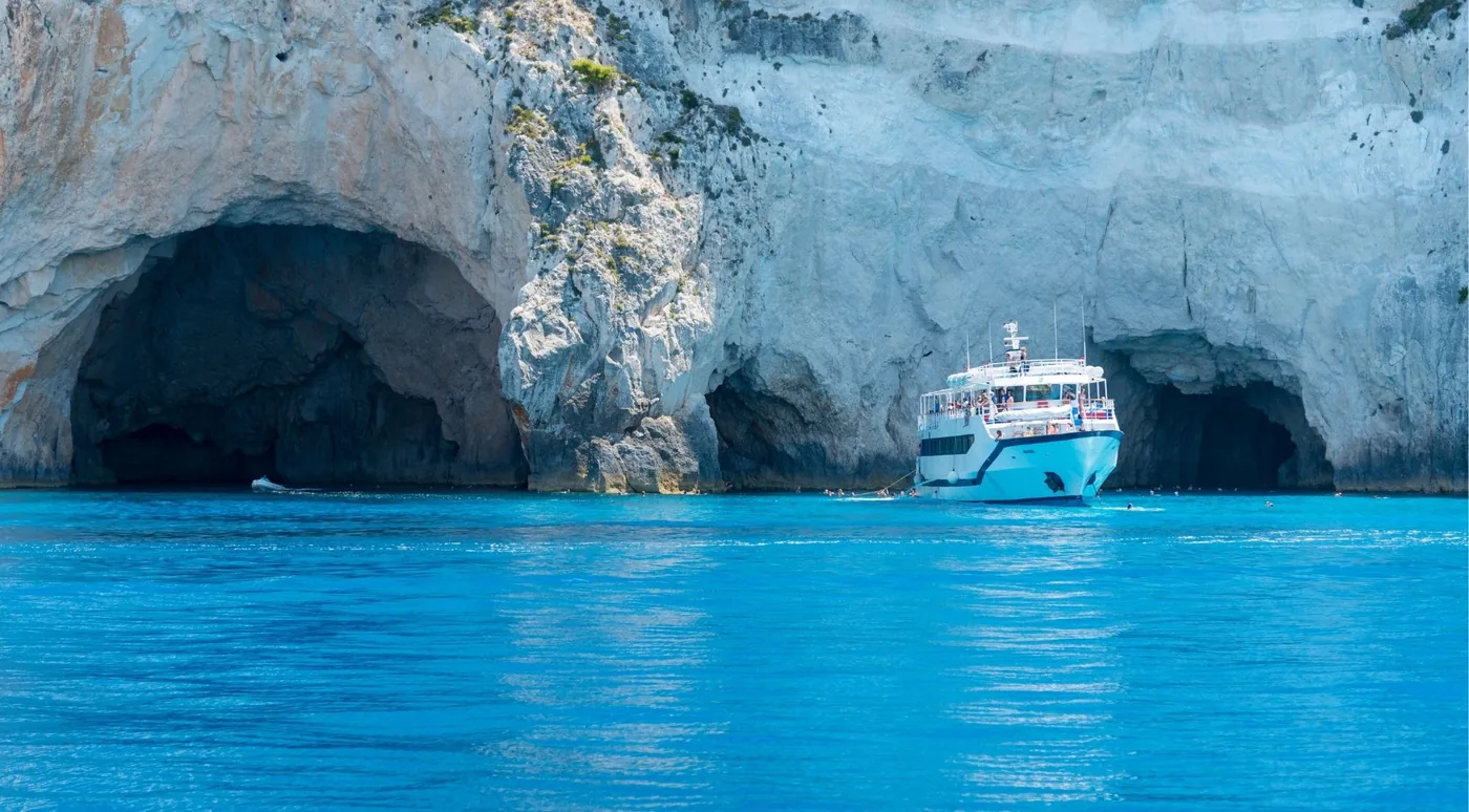 A large excursion boat at the mouth of two big sea caves with swimmers in the water nearby