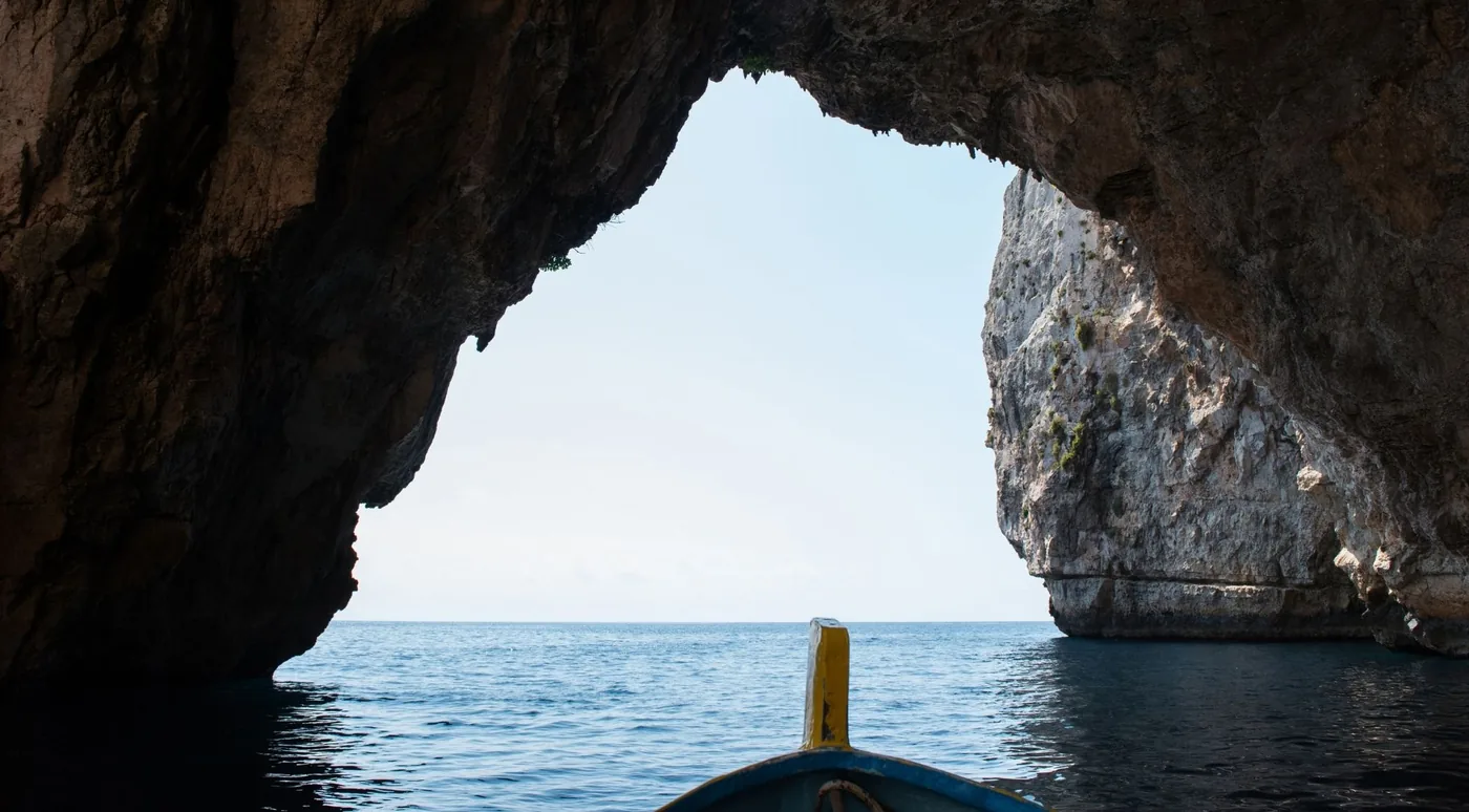 View from inside a sea cave out through its arch, with the bow of a wooden boat in the foreground